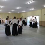 Groups of three students across the mat. Two hold one at either side, and the one drops their weight down.