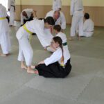One student sitting cross-legged whilst another pushes on their shoulders from the front.